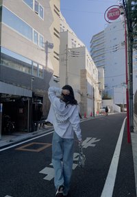 Καθημερινό ντύσιμο με έναν λευκό φούτερ με κουκούλα και φαρδιά μπλε τζιν. Το φόντο δείχνει αστικά κτίρια και πινακίδα δρόμου.