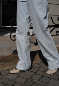 Light blue denim wide-leg trousers with turned-up hems and visible stitching, teamed with beige pointed-toe heels on a cobbled surface.