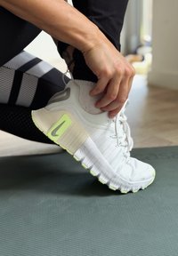 Inimene, kes kannab musti retuuse, reguleerib valget Nike jalgpalli kinga rohelisel treeningumatil siseruumides.