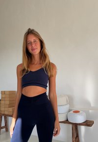 Granatowy prążkowany krótki top i legginsy z wysokim stanem. Charakterystyczne detale to teksturowana tkanina i dopasowana talia. W tle neutralne, utrzymane w stonowanych kolorach siedzisko.