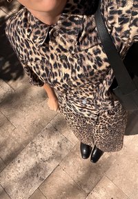 Leopardi mustriga särk ja püksid, valmistatud siledast kangast, millel on krae, nööbid ja mille juurde on sobitatud mustad pahkluu saapad ja kott.