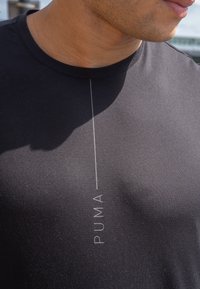 Must have pandud must t-särk, mis on valmistatud sujuvast ja venivast kangast, esiküljel vertikaalse valge "PUMA" logoga. Ümar kaelus.