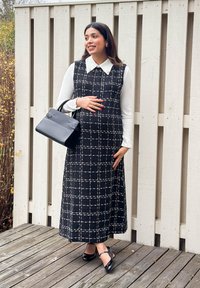 Crno-bijela haljina bez rukava s uzorkom rešetke, s bijelim ovratnikom, uparena s crnom torbicom i cipelama s remenčićem oko gležnja, postavljena na drvenom podu.