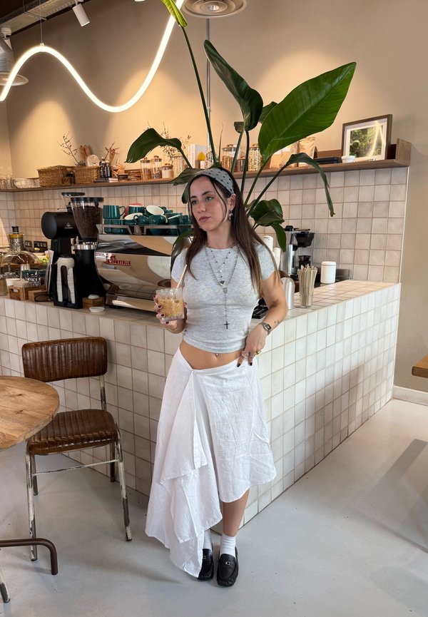 Grå tætsiddende crop top, hvid lagdelt nederdel, sorte loafers og mønstret pandebånd. Baggrunden indeholder en kaffemaskine og en grøn plante.