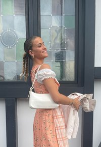 Rosa chiaro con motivo floreale e maniche a volant. Tiene una borsa a mano bianca con stampa cocco e un giubbotto beige piegato.