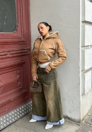 Sudadera corta marrón con detalles en blanco, jeans de pierna ancha verde olivo y un bolso marrón texturizado. Zapatos blancos de puntera en punta con diseño de malla.