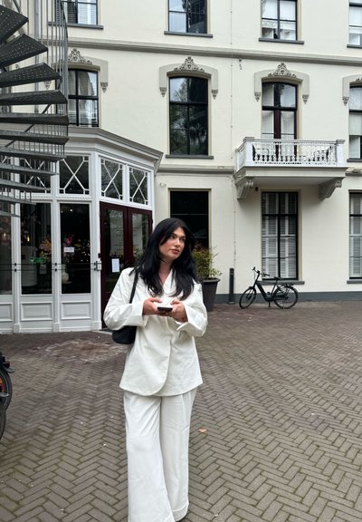 Blazer blanco y pantalones de pierna ancha, combinados con un bolso negro de hombro. Edificio moderno cuenta con grandes ventanas y una escalera de caracol.