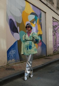 Μαρία blazer σε μέντα πράσινο χρώμα με μπλε σχέδια σε υδατογραφία, σε συνδυασμό με γυαλιστερά ασημί παντελόνια σε φαρδιά γραμμή. Συμπληρωμένο με υπερμεγέθη μαύρα γυαλιά ηλίου.