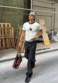 Balta marškinėliai su juodos spalvos žvaigždės dizainu, juodi džinsai ir rudas odinis krepšys. Dėvima su pilka beanie kepure ir juodais batais. Miestovaizdis su medinėmis paletėmis.