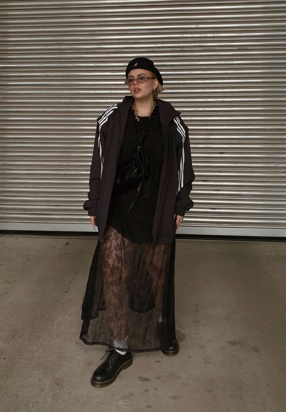 Μαύρο φούτερ με κουκούλα και λευκές ρίγες, επενδυμένο πάνω από ένα μαύρο φόρ εμα με υφή δαντέλας. Μαύρα, χοντρά παπούτσια και γυαλιά ηλίου ολοκληρώνουν το λουκ.