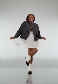 Grey wool cardigan over a white pleated dress, paired with ivory knee-high socks and black ballet flats, on a reflective surface.
