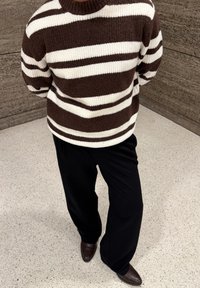 Pull en maille rayé marron et blanc avec un col rond, assorti à un pantalon large noir et des chaussures marron foncé. Tissu texturé visible.