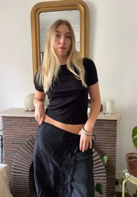 Must värviline lühikeste varrukatega topp, millel on ribade muster, kombineeritud tekstuuriga musta seeliku ja hõbedase käevõruga. Lisaks on looduslik kivi dekoratsioon telliskivi kaminal.