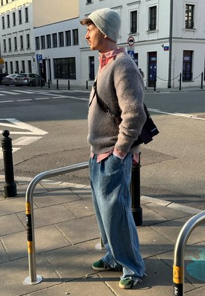 Suéter gris de punto, camisa de color rosa claro con cuello, jeans de mezclilla azul holgados, zapatillas verdes. Un bolso cruzado marrón se lleva sobre el hombro.