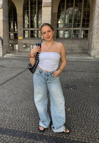 Top bianco senza spalline, jeans a gamba larga azzurri chiari strappati con decorazioni, borsa a tracolla bianca e nera a pois, sandali neri.