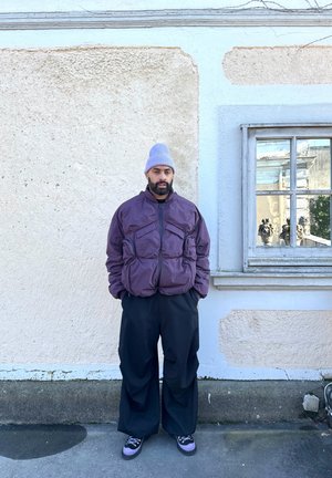 Geacă puf purple cu multiple buzunare frontale, pantaloni largi negri și căciulă gri. Pantofi negri cu accente purple.