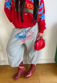 Sweat-shirt rouge avec texte coloré, pantalon de survêtement gris ample avec motif bleu et rouge, bottes de pluie rouges brillantes, et petit sac à main rouge.