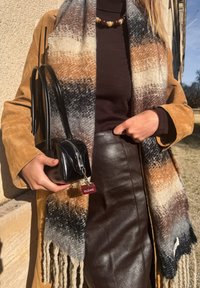 Tan-colored seemisnahast mantel pruuni topi kohal, maatoonides mustriga sall. Must nahast väike kott lukuga ja punase sildiga. Pruun nahast seelik.