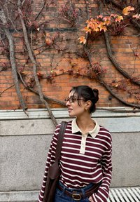 Gestreept shirt met lange mouwen in kastanjebruin en crème, voorzien van een kraag en knopen, gecombineerd met een high-waisted jeans en een bruine schoudertas.