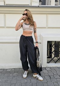 Sportski outfit sastavljen od svijetlosmeđeg crop topa i širokih crnih hlača. Dodaci uključuju uzorčanu torbu i bijele tenisice s bež potplatima.