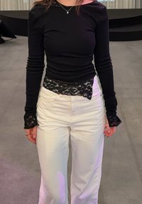 Haut noir à manches longues avec des accents en dentelle à l'ourlet et aux poignets, associé à un pantalon blanc à jambes larges. Texture de tissu lisse avec une coupe ajustée.