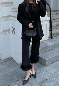 Μαύρο oversized σακάκι, εφαρμοστό τοπ και φαρδιά παντελόνια με τελείωμα από ψεύτικη γούνα. Μαύρες γόβες με δίχτυ και μικρή μαύρη τσάντα.