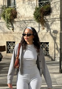 Cardigan gris à côtes sur un ensemble gris ajusté à la texture lisse, complété par des lunettes de soleil noires et un sac en bandoulière marron.