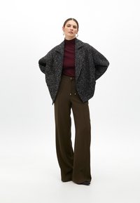 Oversized czarna marynarka Tweed z wielokolorowymi fleckami, noszona na dopasowanym bordowym golfie, w połączeniu z spodniami o wysokim stanem w kolorze oliwkowym.