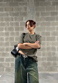 Camiseta de gran tamaño en verde oliva, jeans de mezclilla azul holgados, bolso de cuero negro, hebilla de cinturón plateada, textura ligera con un sutil desgaste.