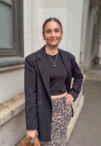 Μαύρο tailored σακάκι πάνω από ένα μαύρο cropped τοπ, συνδυασμένο με φούστα με λεοπάρ σχέδιο. Τα αξεσουάρ περιλαμβάνουν ένα κολιέ με μενταγιόν και μια καφέ τσάντα.