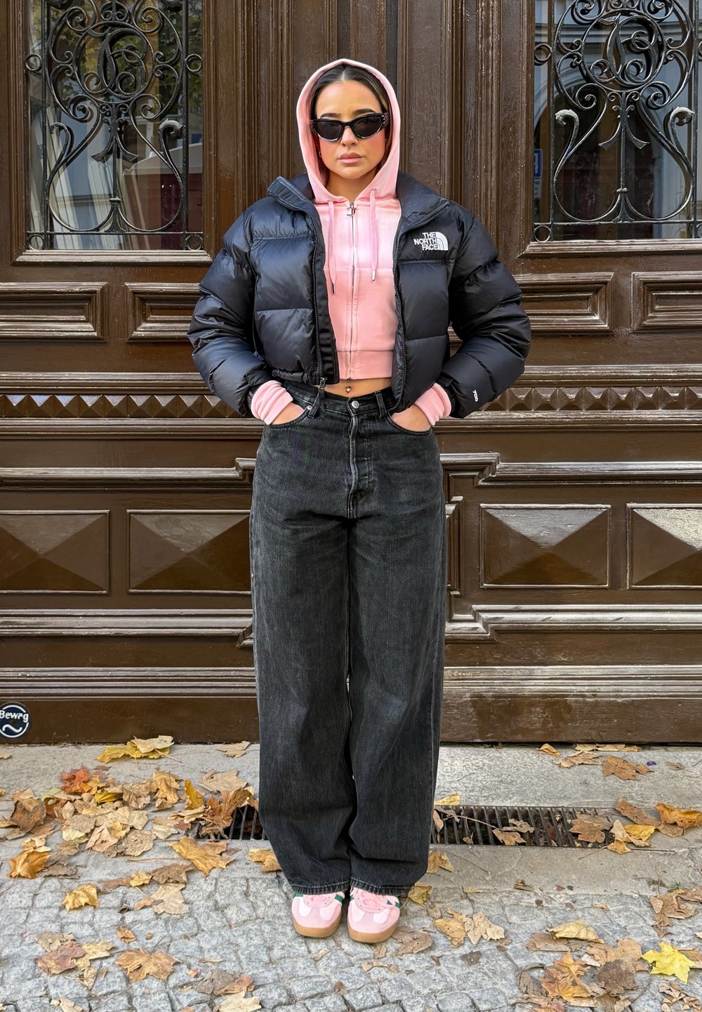 Musta toppatakki, vaaleanpunainen lyhyt huppari, korkeavyötäröiset mustat farkut ja vaaleanpunaiset slip-on-kengät. Tummat, kiiltävät materiaalit ja ylisuurikokoinen leikkaus.