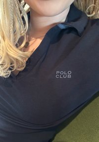 Polo shirt bleu marine avec col et manches courtes, arborant un logo subtil "POLO CLUB" en gris sur la partie gauche de la poitrine. Texture lisse.