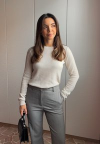 Světlý béžový svetr, šedé kalhoty na míru a černá kabelka. Hladká tkanina, přiléhavý střih a jednobarevné tóny vytvářejí profesionální vzhled.