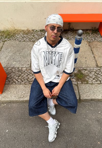Camiseta blanca de Nike con detalles en azul marino, pantalones cortos de denim holgados y zapatillas deportivas plateadas. Una bandana y gafas de sol completan el look.