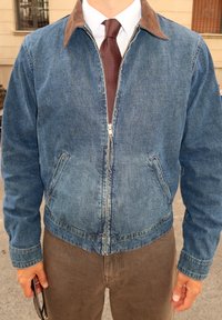 Denim jakk koos pruuni kangaga kraega, lukuga ees, küljetaskudega ja soonikkoes kummipaelaga, koos pruuni lipsu ja beeži pükstega.