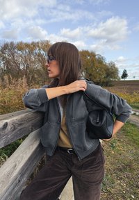 Szara krótka bluza z kapturem i zamkiem z przodu, noszona na beżowej bluzce. Połączona z ciemnobrązowymi sztruksowymi spodniami i małą czarną torebką.