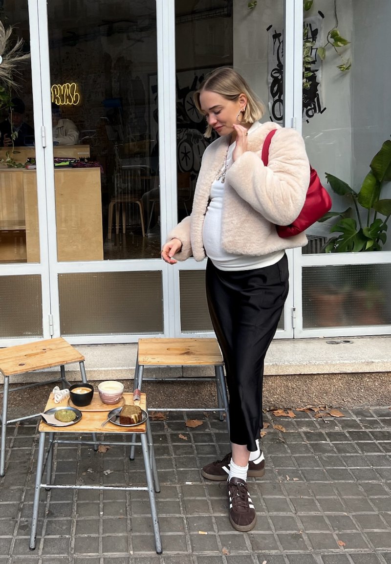 Ταν ψεύτικη γούνα μπουφάν, άσπρη μπλούζα, μαύρο σατέν παντελόνι και καφέ αθλητικά παπούτσια. Δύο ξύλινες σέλες με κεραμικά μπολ και μια φέτα ψωμί πάνω τους.