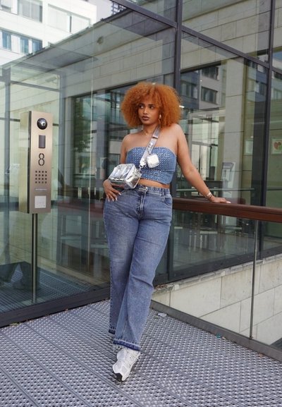 Top corto de denim con acentos de cuentas, jeans azules de cintura alta y un bolso cruzado metálico plateado. Zapatillas blancas completan el look.