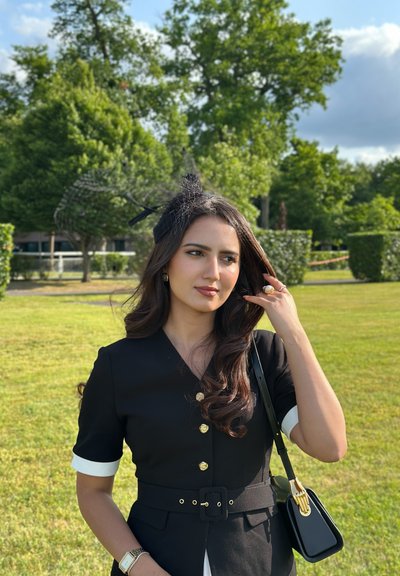 Vestido negro con puños blancos, botones dorados, cintura ceñida, combinado con un bolso negro con herrajes dorados y una diadema decorativa.