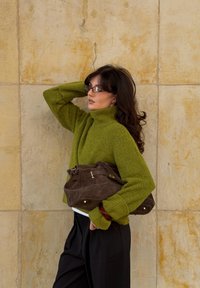 Grøn strikket turtleneck sweater, loose fit, struktureret materiale. Brun ruskinds håndtaske med guldfarvet hardware. Sorte bukser med vidde.