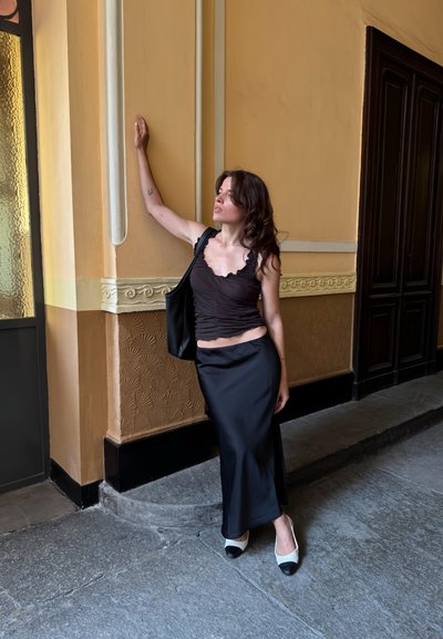 Top negro con fruncidos y bordes con volantes, combinado con una elegante falda maxi negra. Acentuado con zapatos bicolores en blanco y negro.