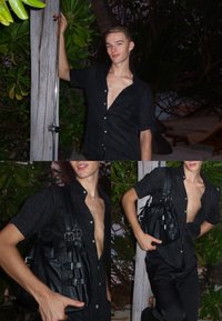 Camiseta preta de manga curta com padrão texturizado, usada desabotoada, combinada com calças pretas. Segura-se uma bolsa preta de couro com fivelas.