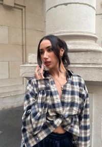 Koszula w kratę o dużym rozmiarze w granatowym i kremowym kolorze, krótki krój, zestawiona z ciemnymi sportowymi spodniami. Gładka tekstura, casualowy design.