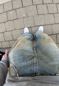 Ανοιχτό μπλε τζιν με φθορά, με χαλαρή εφαρμογή και ορατούς λεκέδες. Οι λεπτομέρειες περιλαμβάνουν μια ασημένια φερμουάρ και μια ετικέτα μάρκας στο μπροστινό μέρος.