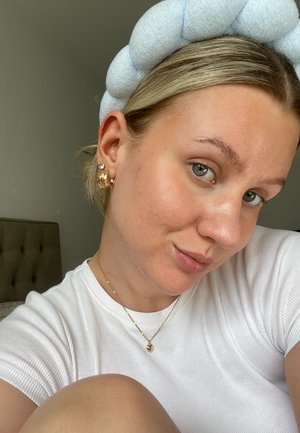 Bandeau en tissu bleu clair, chemise blanche à rayures, boucles d'oreilles en or et perles, collier en or à plusieurs couches avec pendentif en forme de cœur, teint clair, pose détendue.