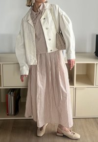 Fehér farmerdzseki egy barna és fehér csíkos hosszú ruhán, bézs cipőkkel párosítva. Kiegészítők között szerepel egy textúrált táska és fülbevalók.