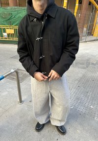 Čierna bunda s uzávermi na cvoky, doplnená svetlosivými oversized teplákmi a čiernymi čižmami. Ležérny mestský outfit zameraný na pohodlie.