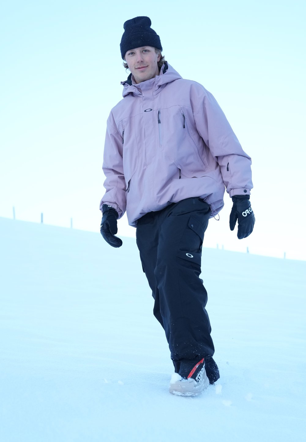 Pink waterproof jacket, black snow trousers, and gloves, worn while walking on snow; features a logo and a loose fit for ease of movement.