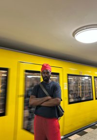 Personne portant un bonnet rouge et une chemise bleue avec un short rouge pelucheux se tient devant un train jaune avec des accents noirs.