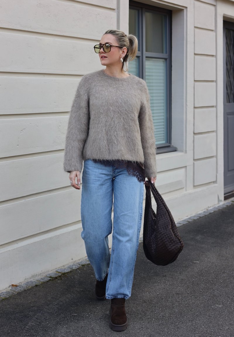 Maglione peloso marrone chiaro, jeans blu a gamba larga, stivali marroni con tacco e borsa marrone con texture. Occhiali da sole e orecchini a cerchio completano il look.